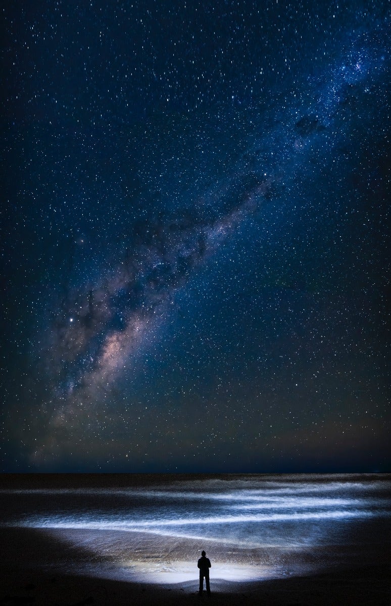 The Milky Way over person on the beach and waves